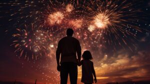 A father holding his little daughter's hand watches a fireworks display.