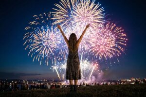 Young woman with raised arms celebrating and watching a spectacular fireworks display at night