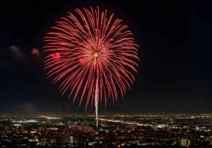 Spectacular Red Fireworks Display Over Urban Cityscape at Night Celebrating Festival Holidays and Independence Day